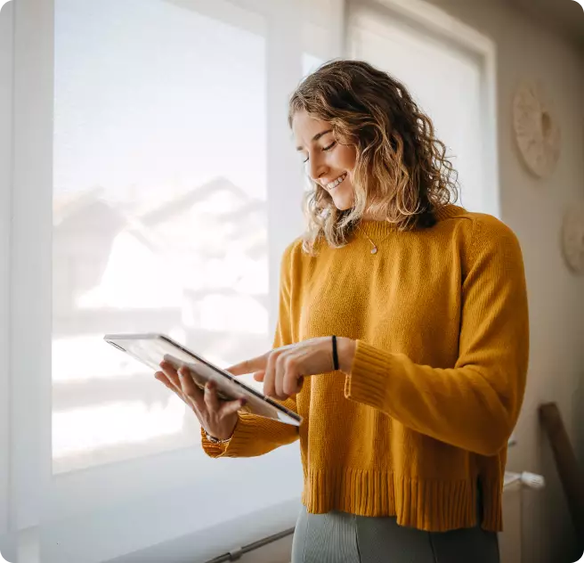 Ein Mann mit Brille und gelbem Hemd lächelt, während er auf sein Smartphone schaut. Im Vordergrund steht eine grüne Tasse auf einem Tisch.