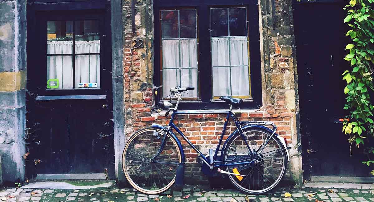 Ein blaues Fahrrad steht angelehnt an eine alte Hausmauer vor der Eingangstür.