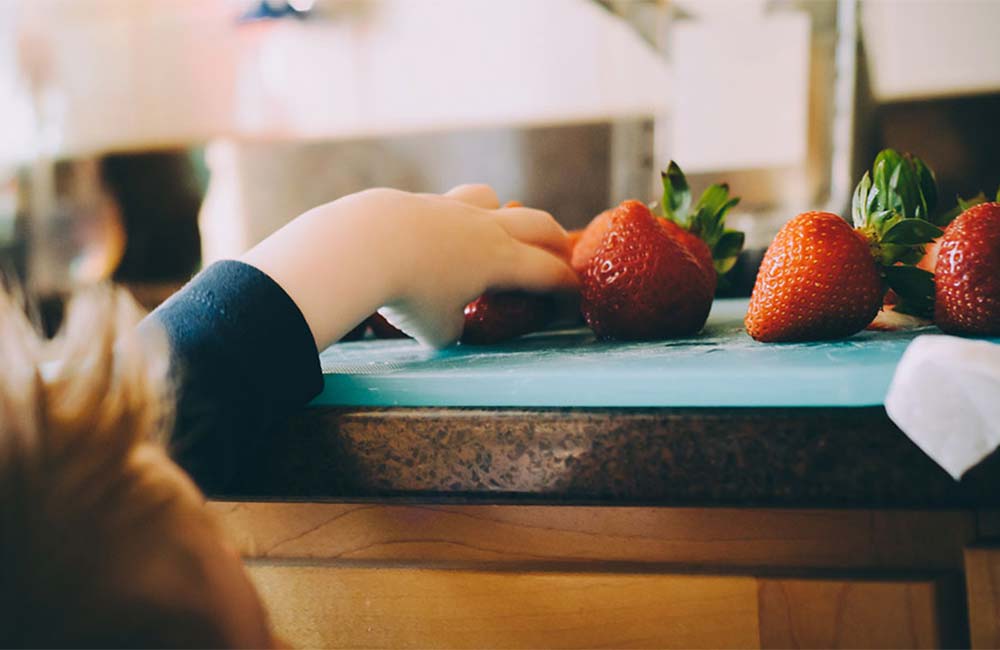 Ein kleines Kind greift nach einer Erdbeere auf einer Küchenarbeitsplatte.