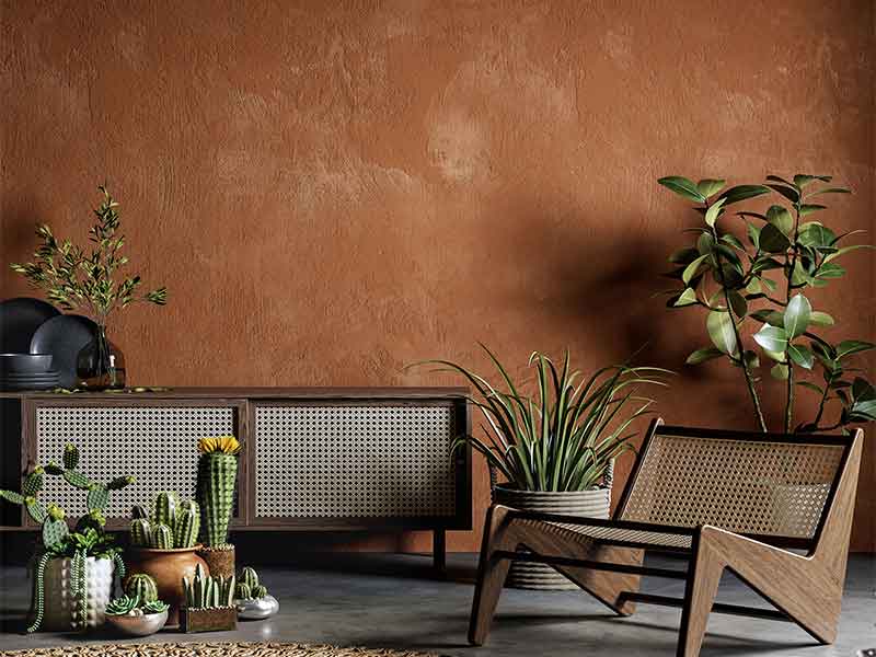 Mit Flechtwerk verarbeitete Möbel und verschiedene Grünpflanzen stehen vor einer mit cognacfarbenem Lehmputz verputzten Wand.