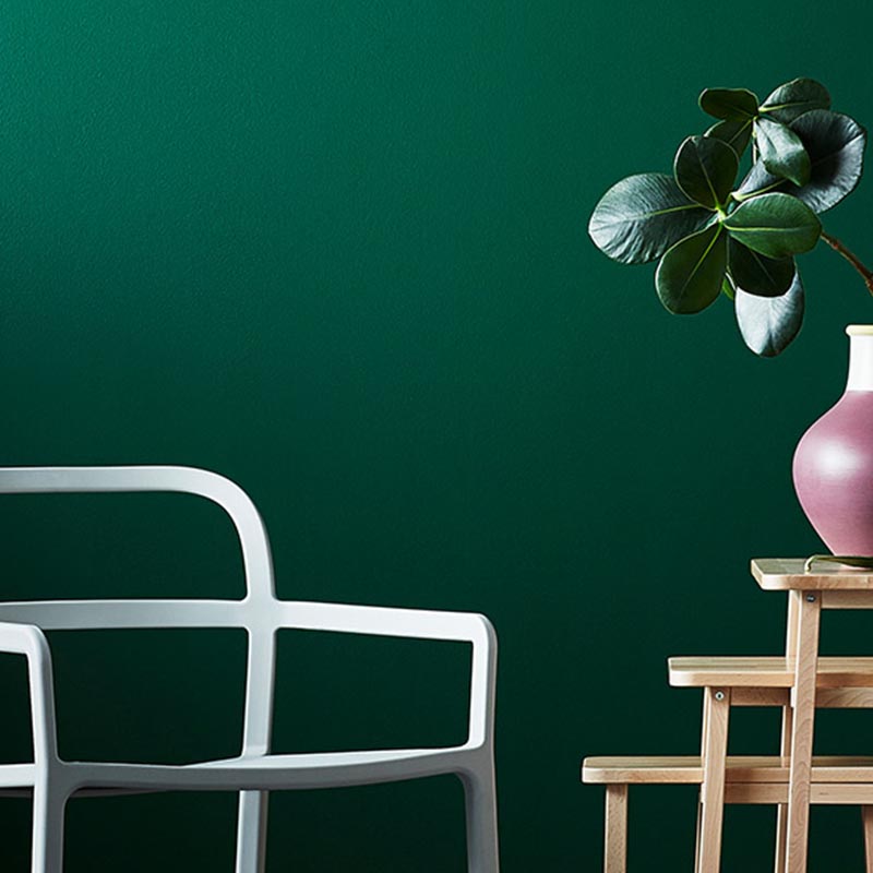 Vor einer dunkelgrün gestrichenen Wand stehen mehrere Holzhocker und ein Stuhl.