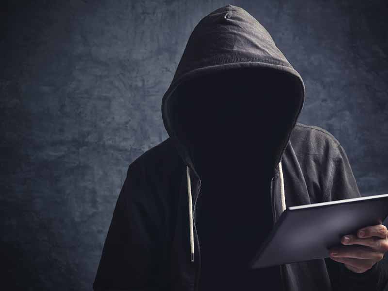 Eine mit einem dunklen Kaputzenpulli gekleidete Person mit unkenntlichem Gesicht hält ein Laptop in der Hand