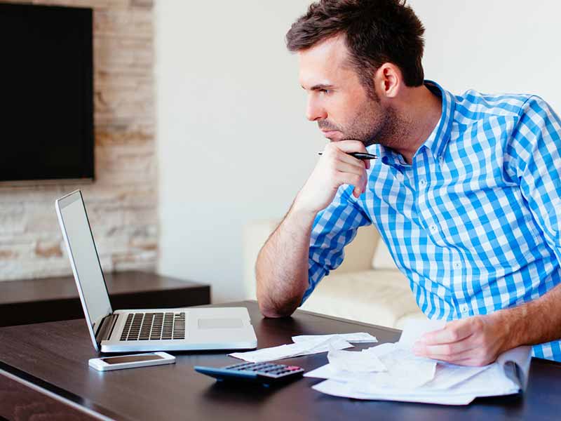 Ein Mann sitzt an einem Schribtisch und sieht konzentriert auf den Monitor seines Laptops.
